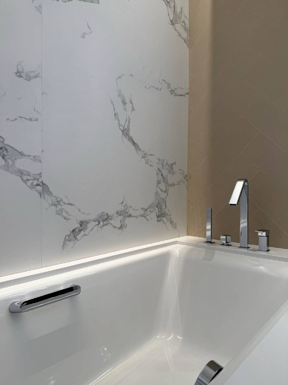 Modern bathroom with a white bathtub in the center. The bathtub has a silver faucet and a silver handle on the right side.