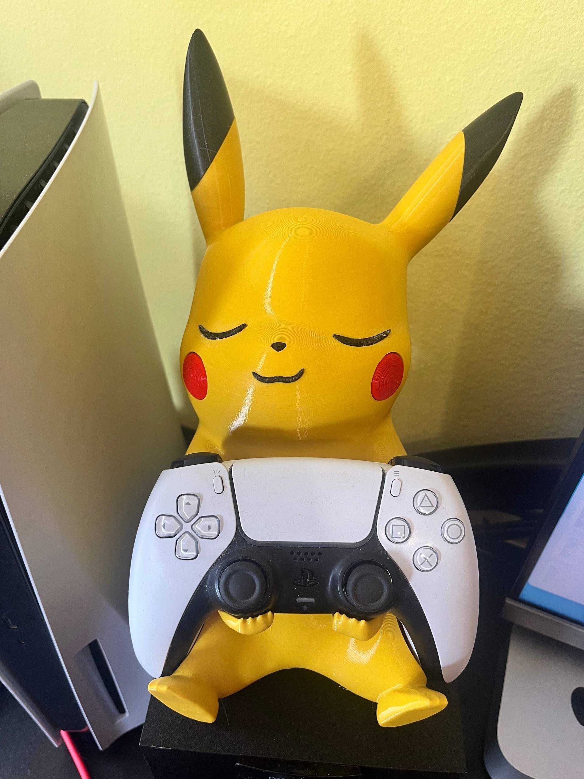Small figurine of the popular Pokemon character Pikachu. Pikachu is sitting on top of a white gaming controller. Pikachu has