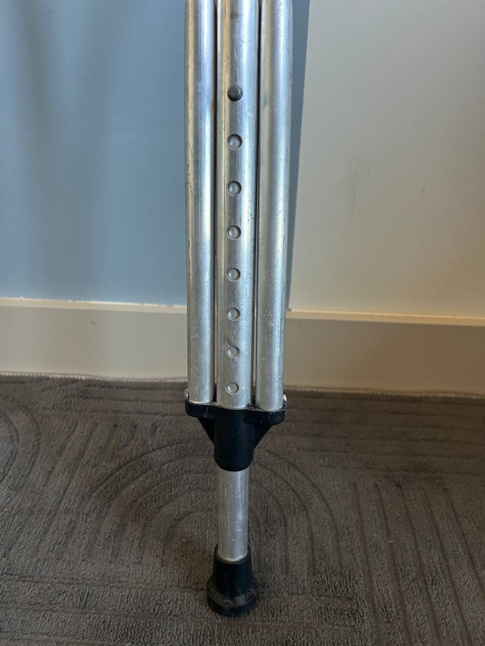 Close-up of a metal pole with a black base. The pole appears to be made of aluminum and has multiple holes on its surface.