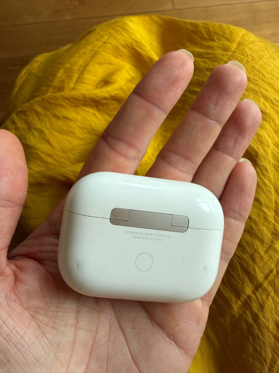 Person's hand holding a small white electronic device. The device appears to be a wireless earbud, as it has a rectangular