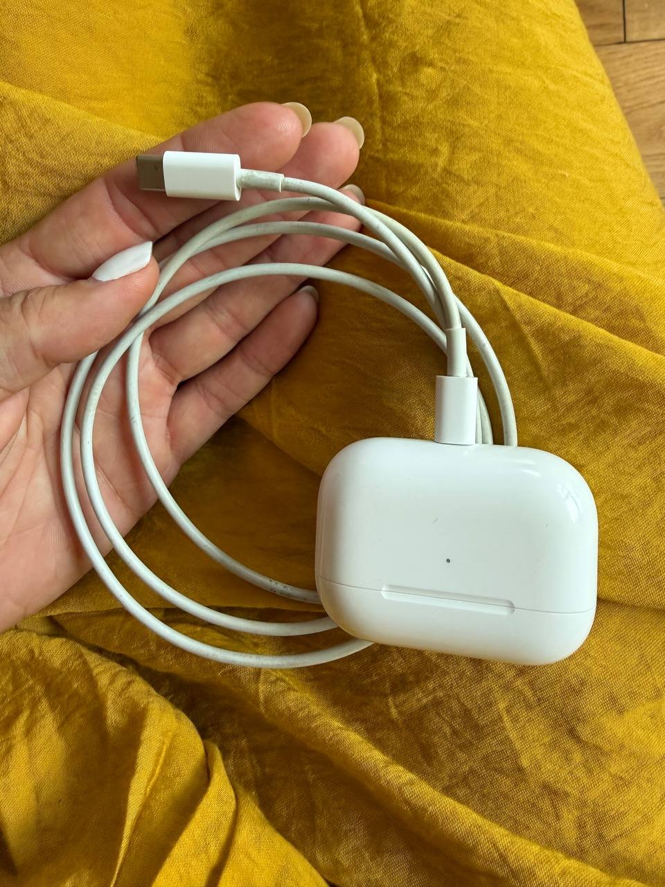 Hand holding a white USB cable. The cable is coiled up and appears to be new. The hand is resting on a yellow fabric