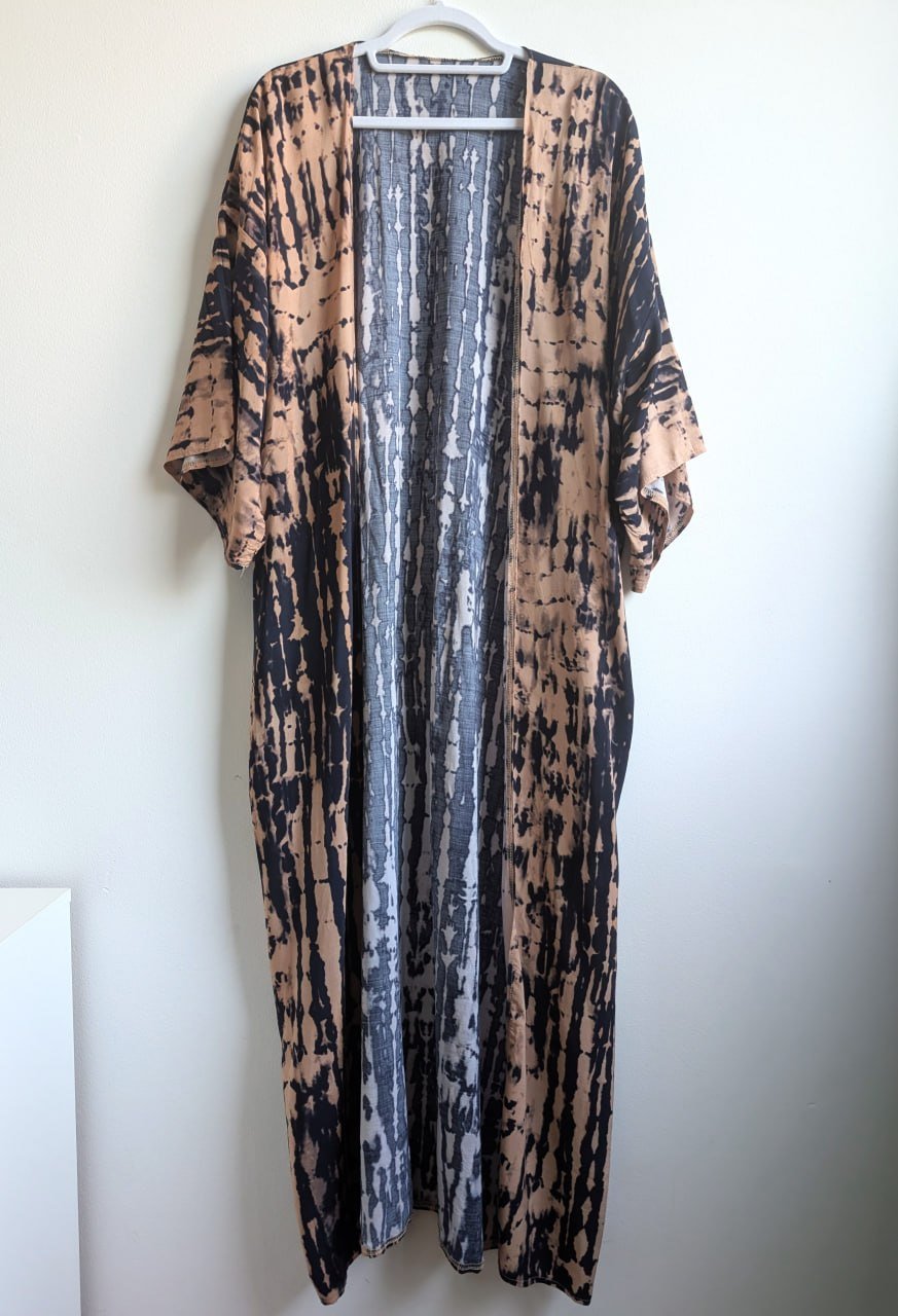 Long, flowing dress hanging on a white hanger against a white wall. The dress is made of a lightweight fabric with a unique