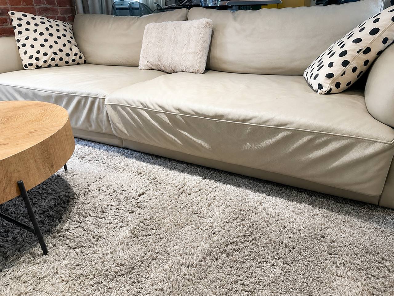 Beige sofa in a living room with a wooden coffee table on the left side. The sofa has three throw pillows on it, one with