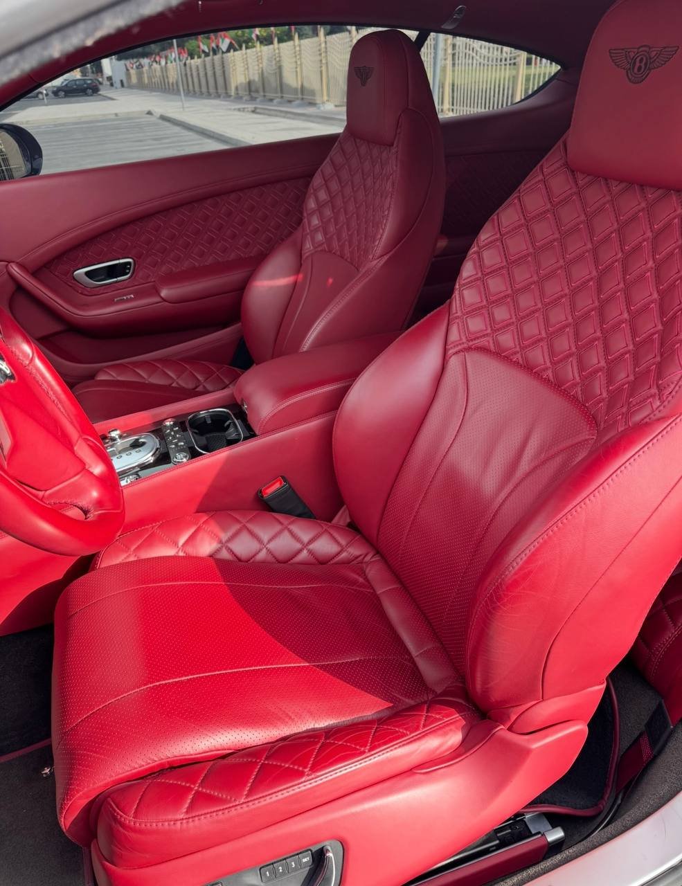 Interior of a luxury car, specifically the front seats. The seats are made of red leather with a quilted pattern and have