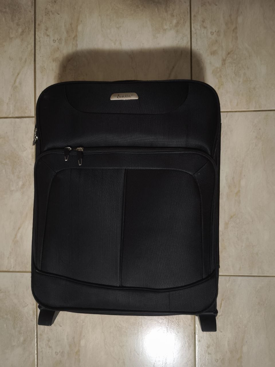 Black suitcase lying on a tiled floor. The suitcase appears to be made of a hard material and has a rectangular shape with
