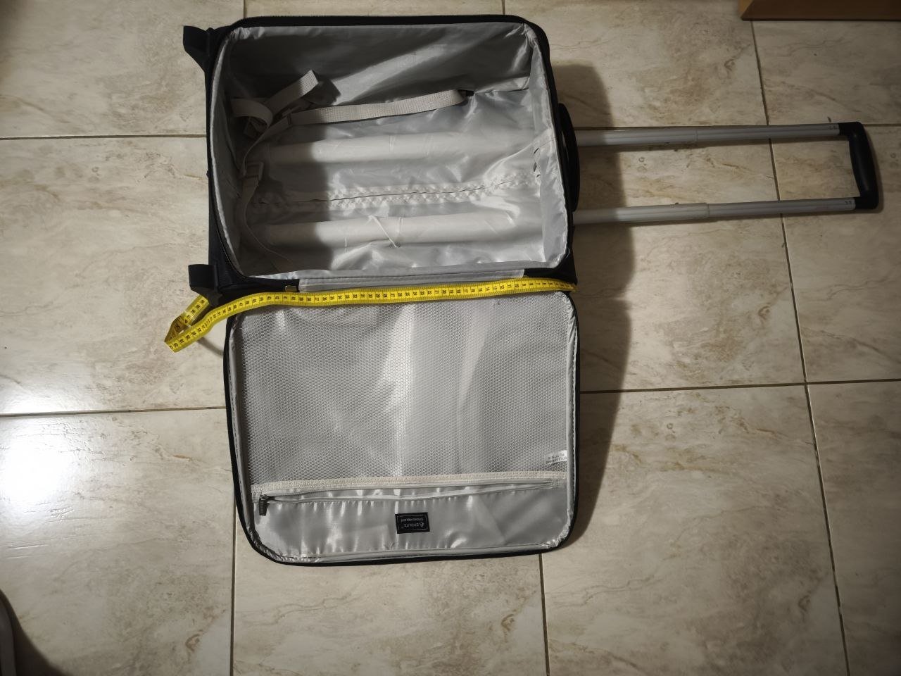 Black suitcase with a handle on a tiled floor. The suitcase is open, revealing the interior of the suitcase. Inside the