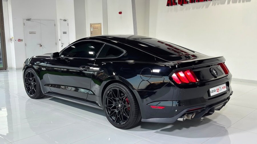 Black Ford Mustang parked in a showroom. The car is a two-door coupe with a sleek and sporty design. It has a long hood and