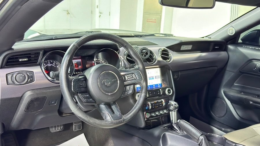 Interior of a car, specifically the driver's seat and dashboard. The car appears to be a Ford Mustang, as indicated by the