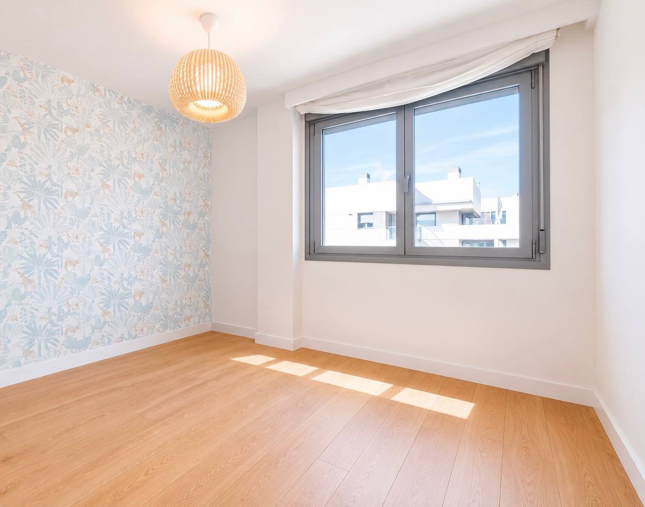Empty room with wooden flooring and white walls. The room has a large window on the right side of the image, which has a