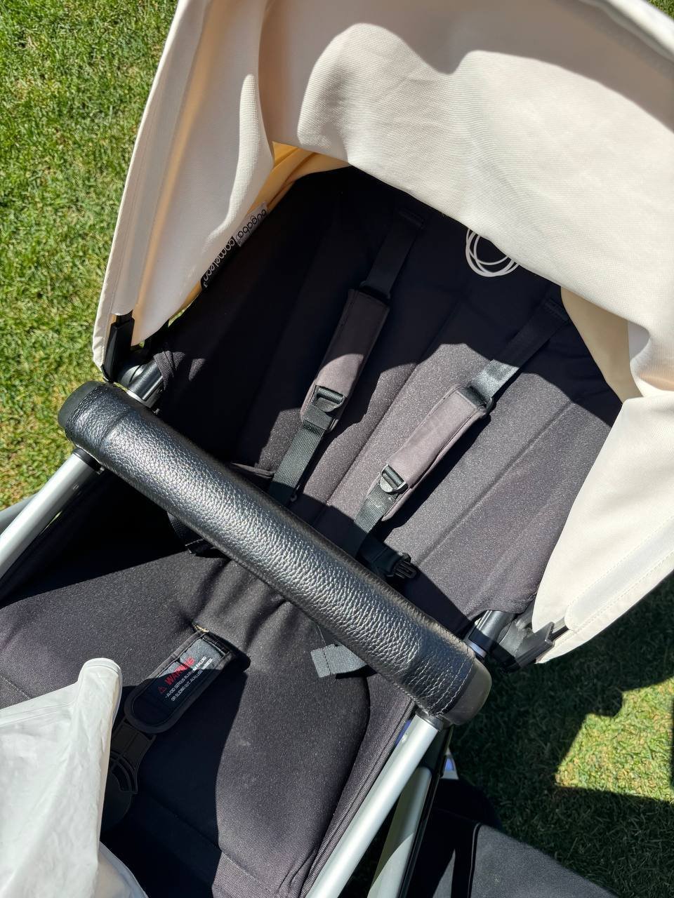 Interior of a stroller with a beige canopy. The stroller has a black seat with two black seat belts attached to it. The