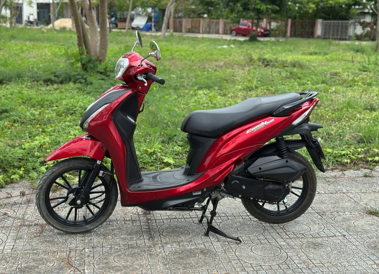 Red and black scooter parked on a concrete pavement in a park. The scooter has a sleek design with a black seat and a red