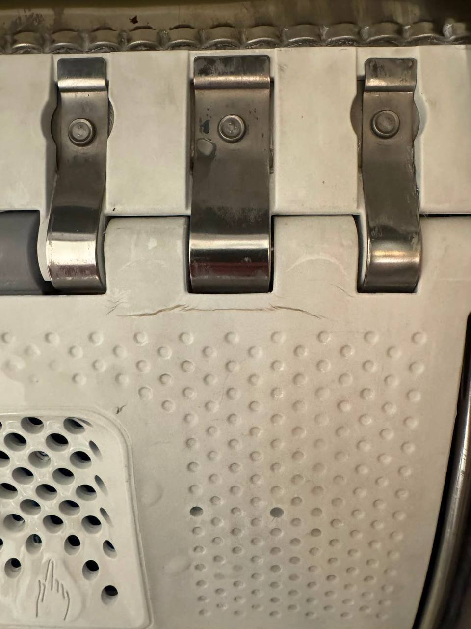 Close-up of a metal latch on a white surface. The latch is made of stainless steel and has two metal latches on either side.