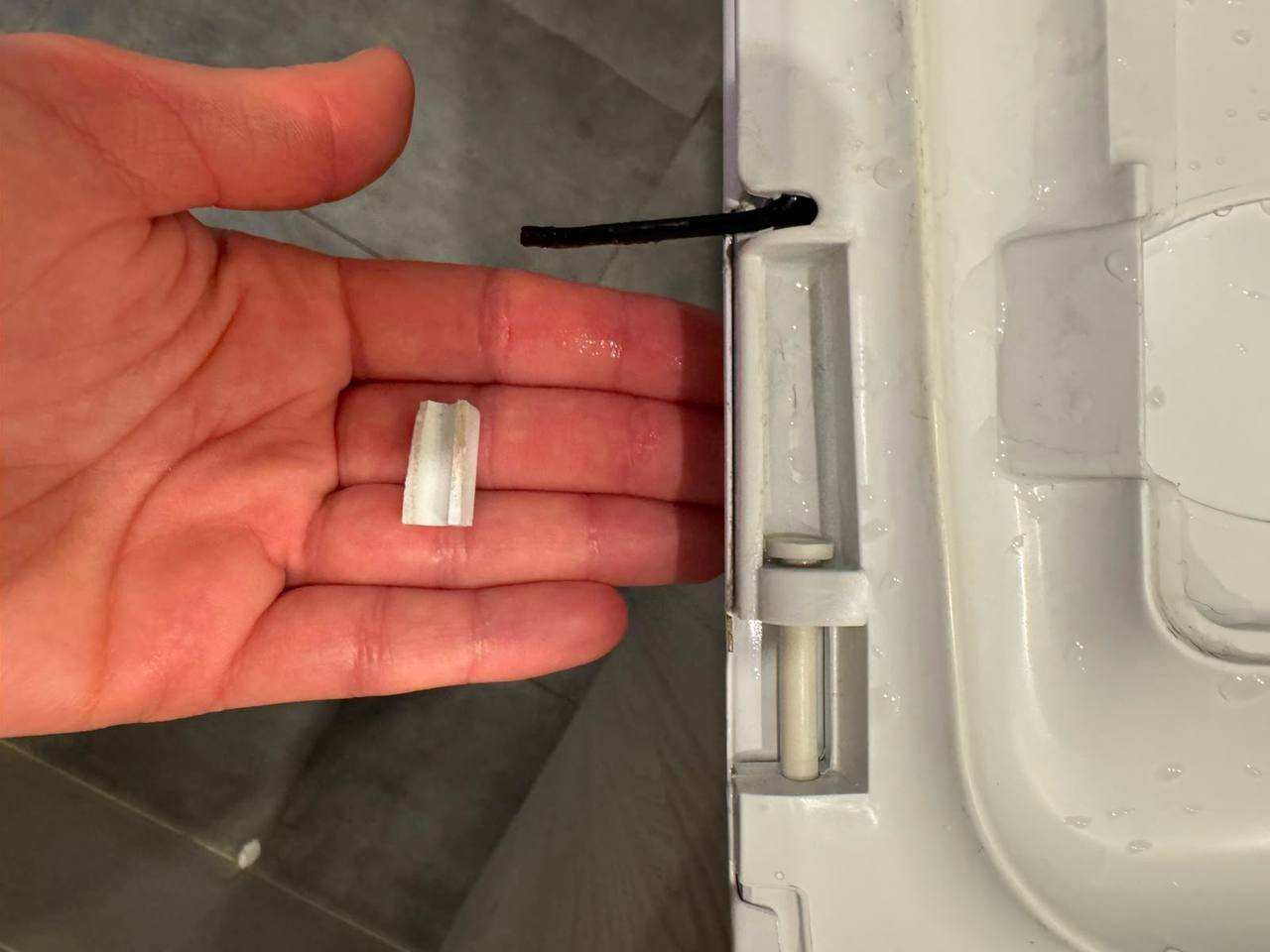 Hand holding a small piece of white adhesive tape in front of a white door. The door appears to be open, as there is a small
