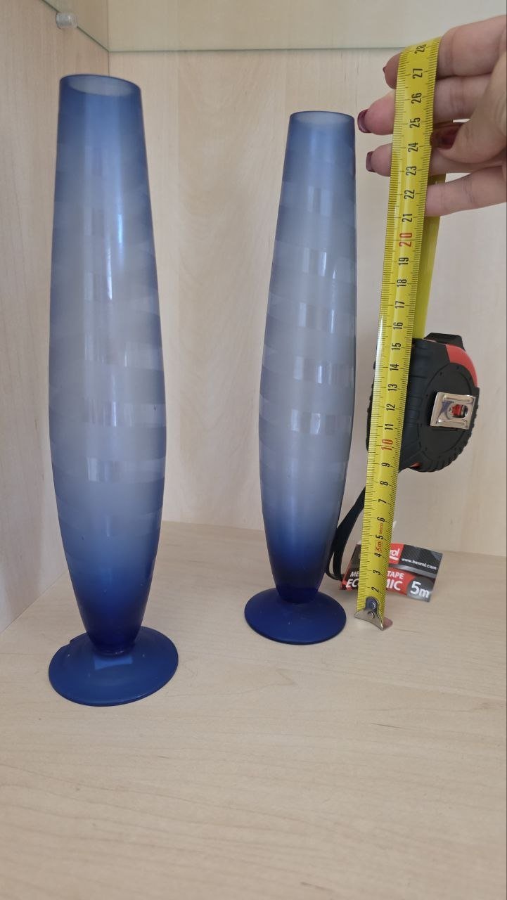 Two tall, blue vases sitting on a wooden surface. The vases are tall and slender, with a wide base and a narrow neck. They