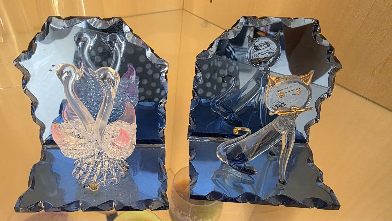 Two glass figurines on a blue base. The figurines are in the shape of a hexagon with a scalloped edge. On the left side of