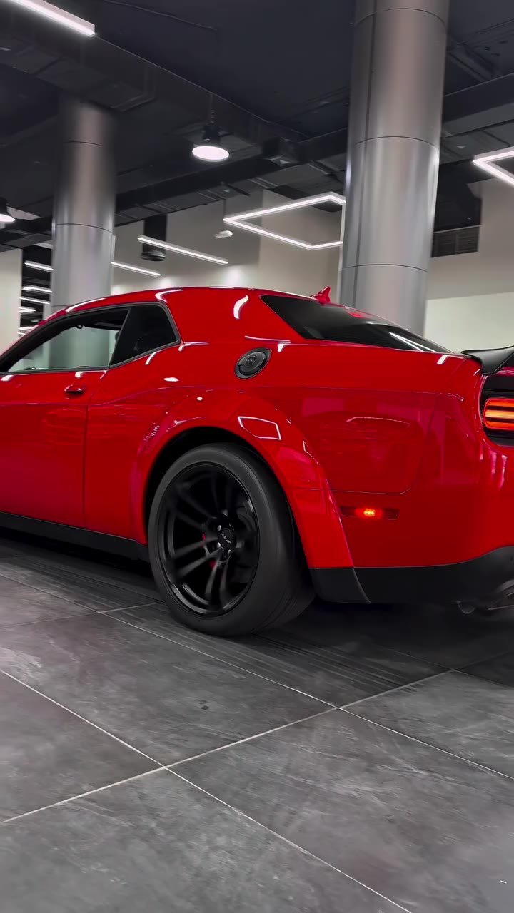 Red sports car parked in a modern garage. The car is a Dodge Challenger, with a sleek and sporty design. It has a black roof