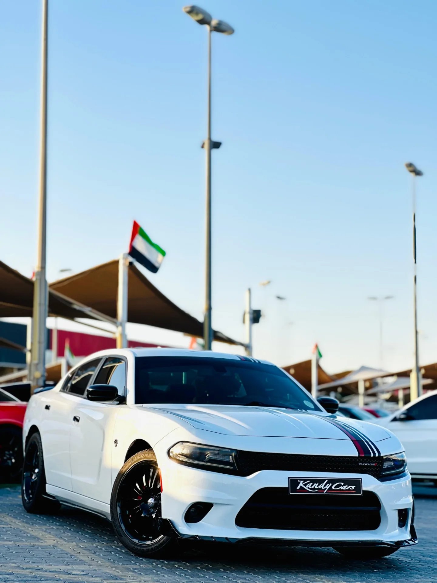 White Dodge Charger car parked in a parking lot. The car is a four-door sedan with a sleek and sporty design. It has a black