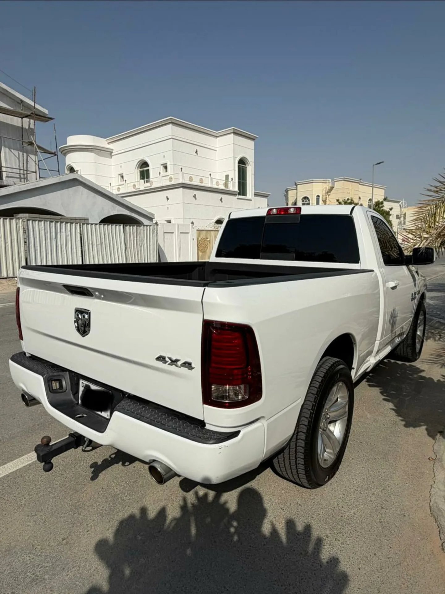 White pickup truck parked on the side of a road. The truck is a Dodge Ram with a black bed cover and a red tail light. It