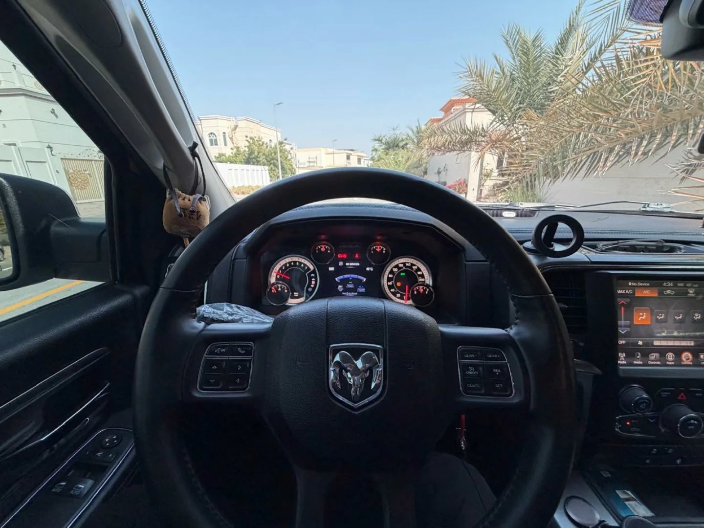 Interior of a car, specifically the driver's seat and dashboard. The steering wheel is black with the Dodge logo in the