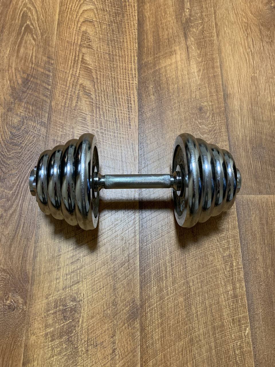 Pair of dumbbells lying on a wooden floor. The dumbbell on the left is made of metal and has a hexagonal shape with a flat