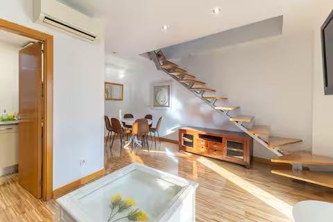 Modern and spacious living room with a wooden staircase on the right side. The staircase has a wooden handrail and a wooden