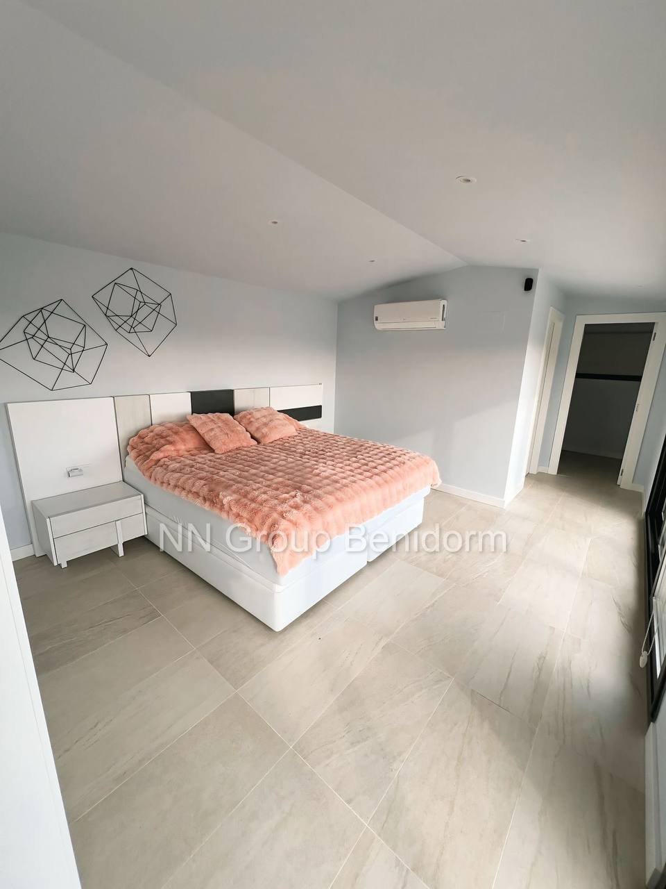 Modern and minimalist bedroom with a large white bed in the center. The bed has a white headboard and footboard, and is