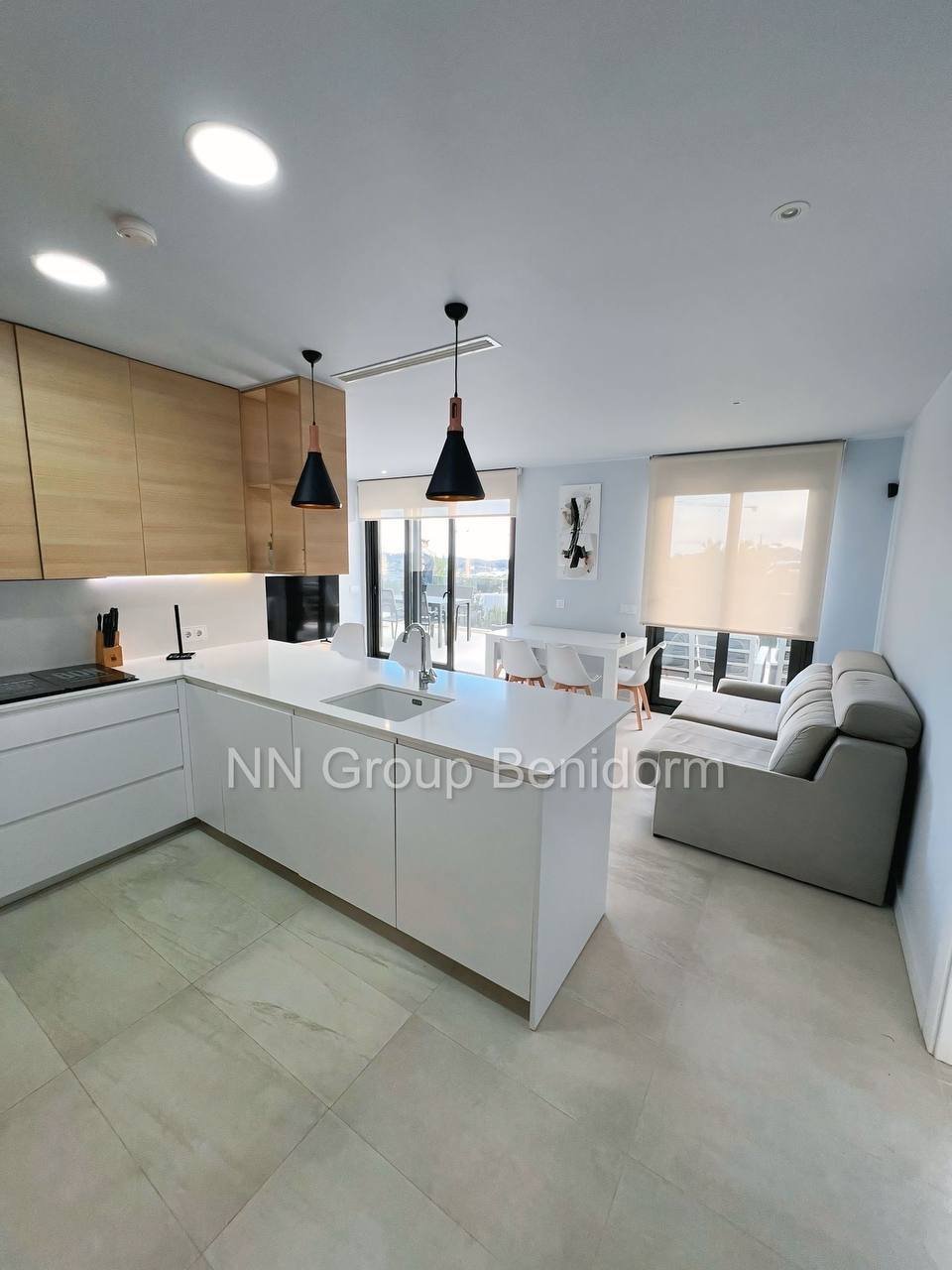 Modern kitchen and living area in a modern apartment. The kitchen has a large island with a white countertop and a sink, and