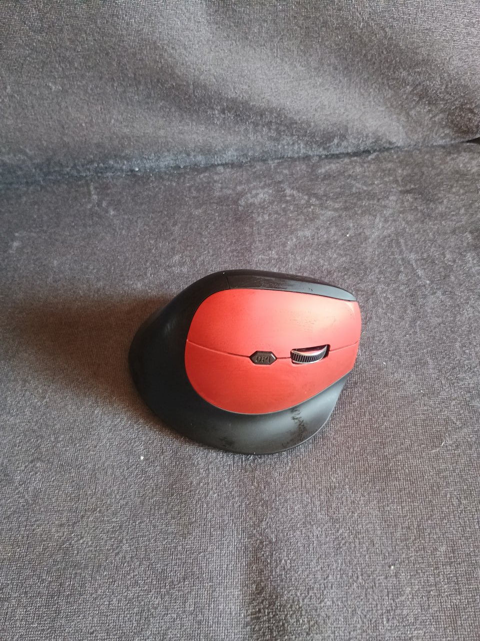 Red and black computer mouse resting on a gray surface. The mouse has a round shape with a flat base and a curved top. The
