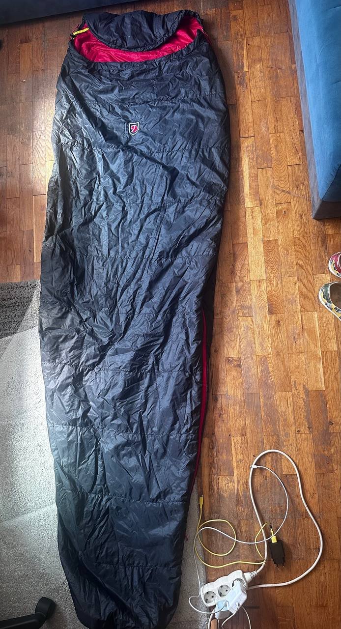 Black sleeping bag lying on a wooden floor. The sleeping bag is made of a waterproof material and has a red zipper on the
