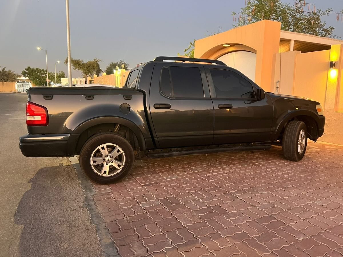 Black pickup truck parked on a brick pavement in front of a building. The truck is a Ford Ranger, with a long bed and a