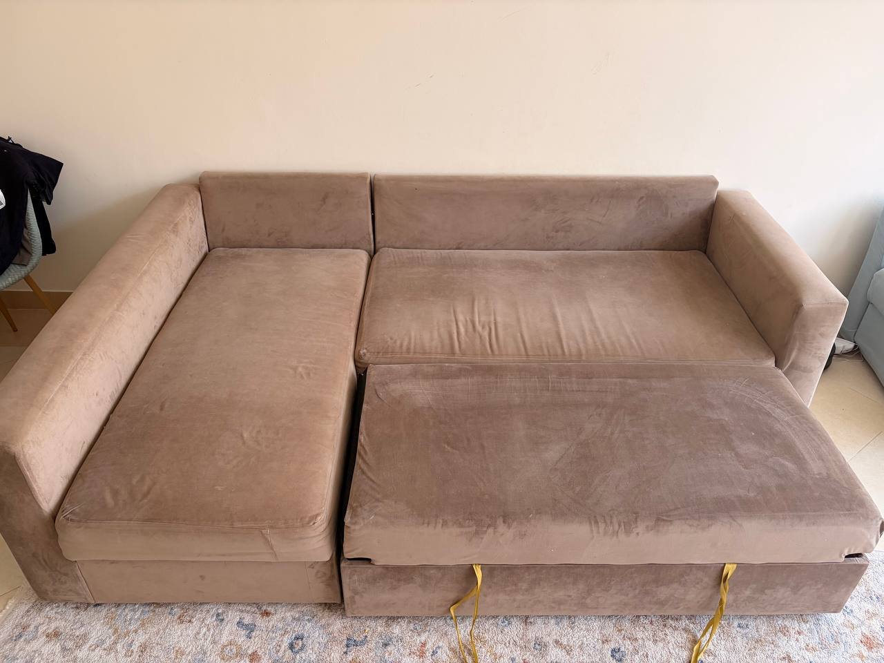 Beige-colored sofa in a room with a white wall and a blue and white patterned rug. The sofa has a modern design with a