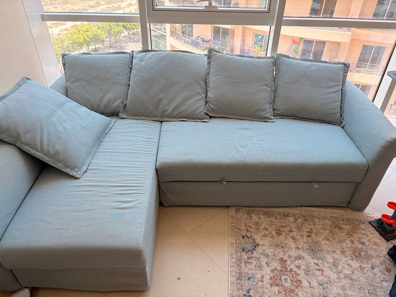 Light blue sectional sofa in a living room with a large window in the background. The sofa has a chaise lounger on the left