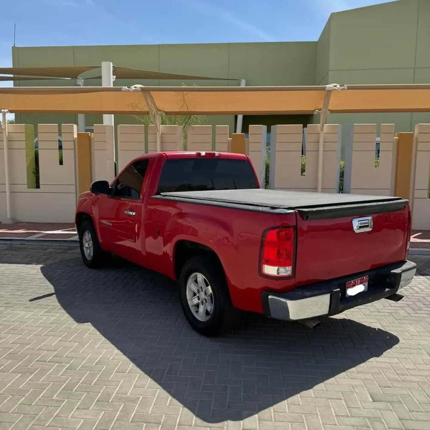 Red pickup truck parked in a parking lot. The truck is a GMC Sierra 1500 pickup truck with a black bed cover on the back. It