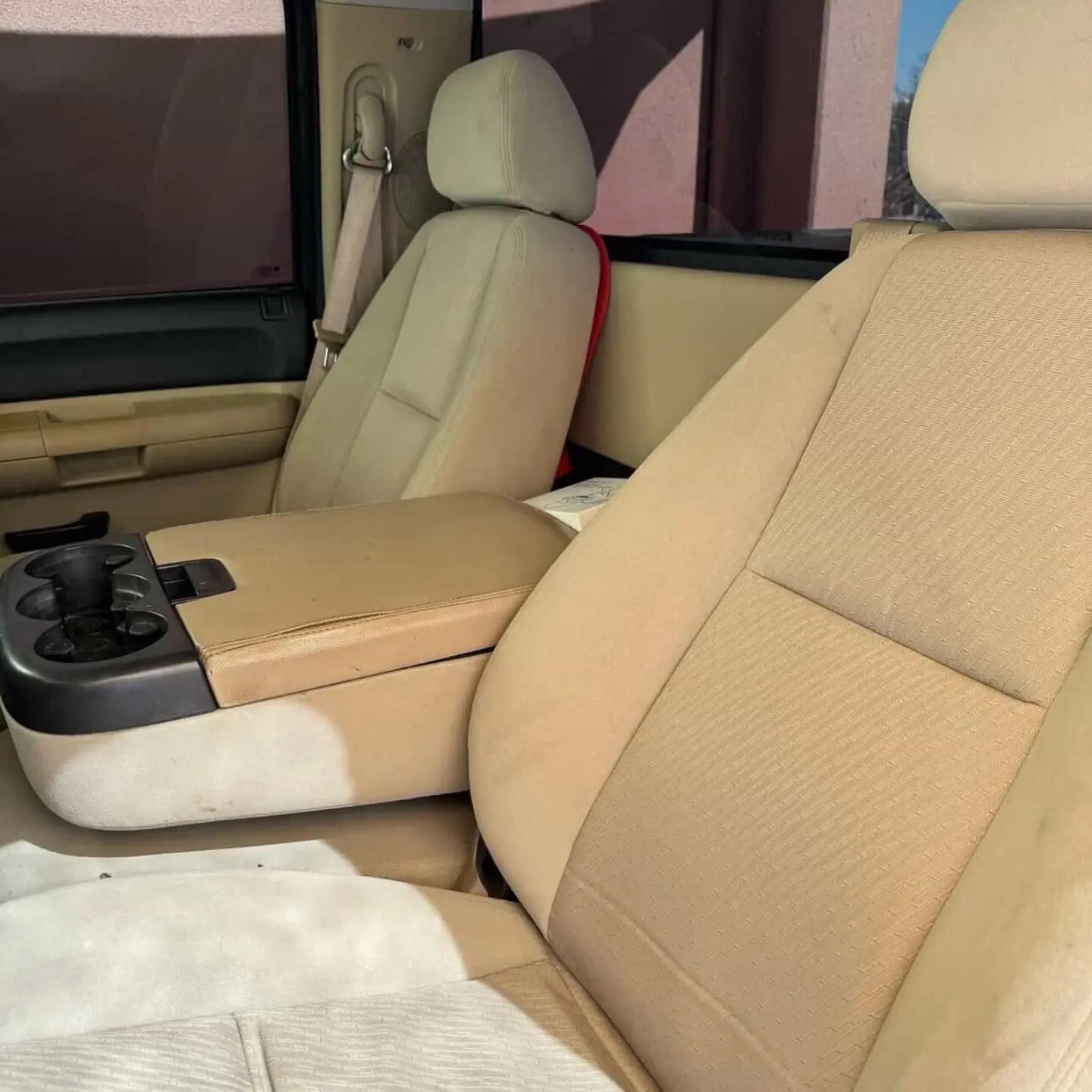 Interior of a car, specifically the back seat. The seat is beige in color and has a cup holder in the center console. The