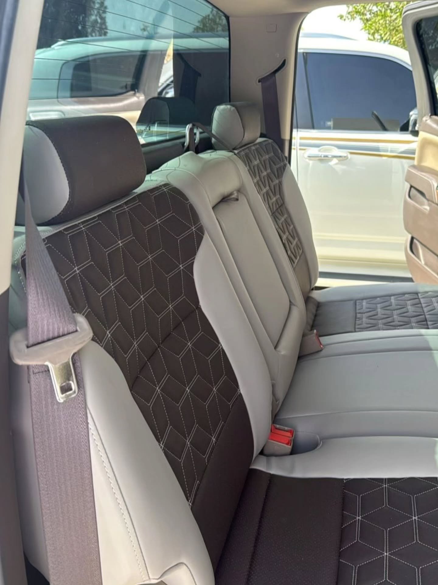 Interior of a car, specifically the back seat. The seat covers are beige in color and have a geometric pattern on them. The