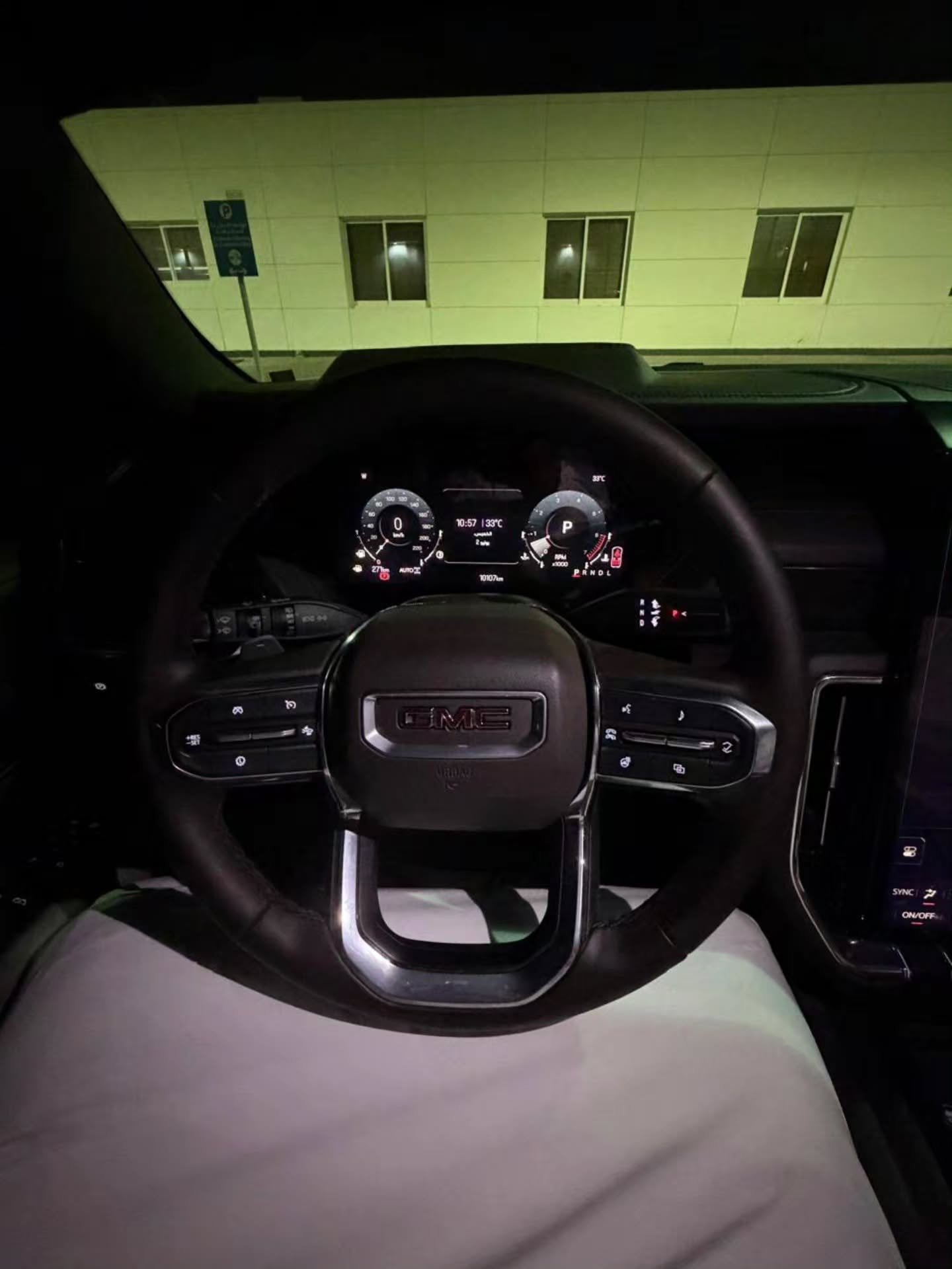 Interior of a car, specifically the driver's seat and dashboard. The steering wheel is black with the GMC logo in the