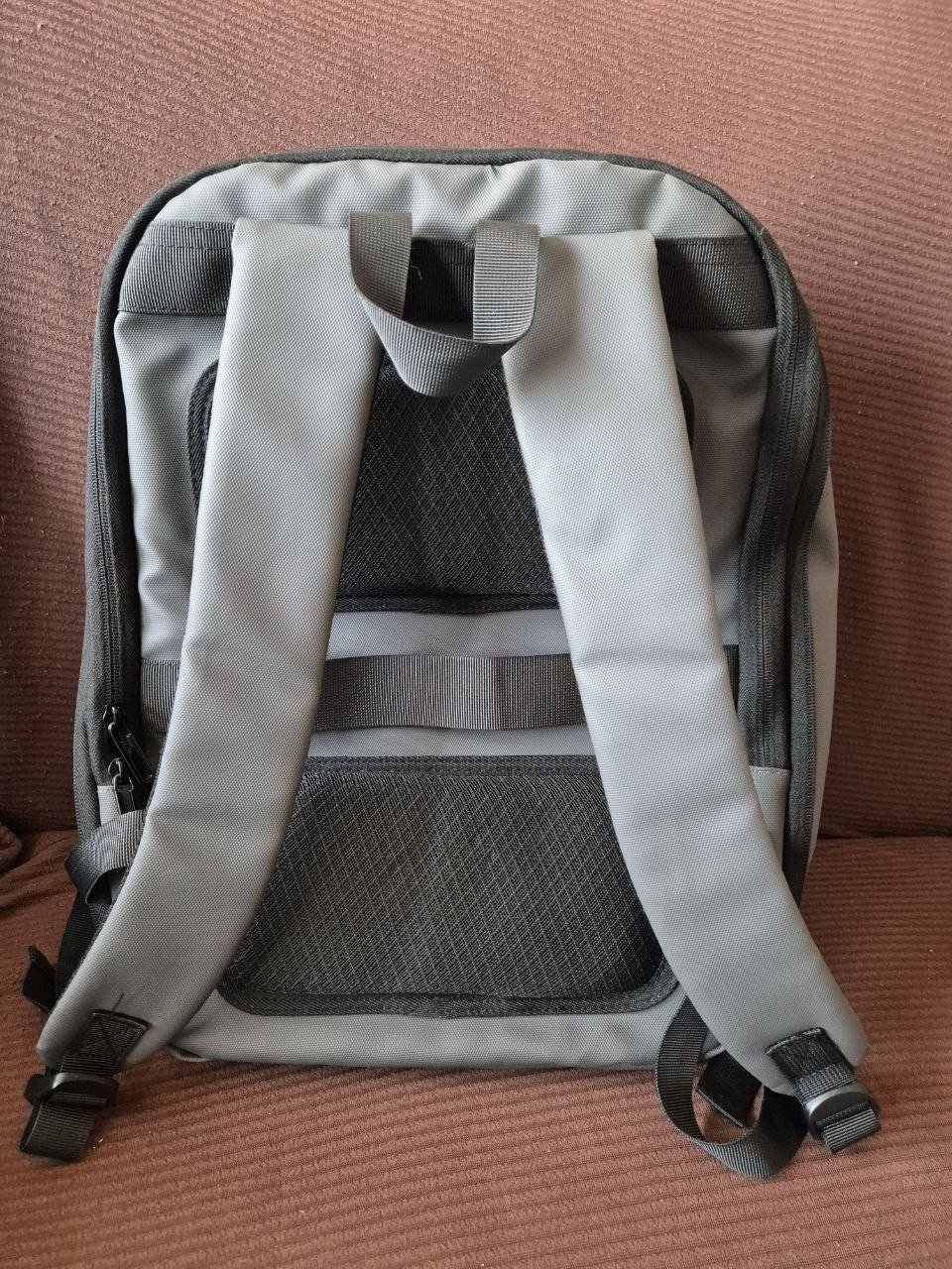 Gray backpack with a black mesh pocket on the front. The backpack has two adjustable straps that are attached to the top of