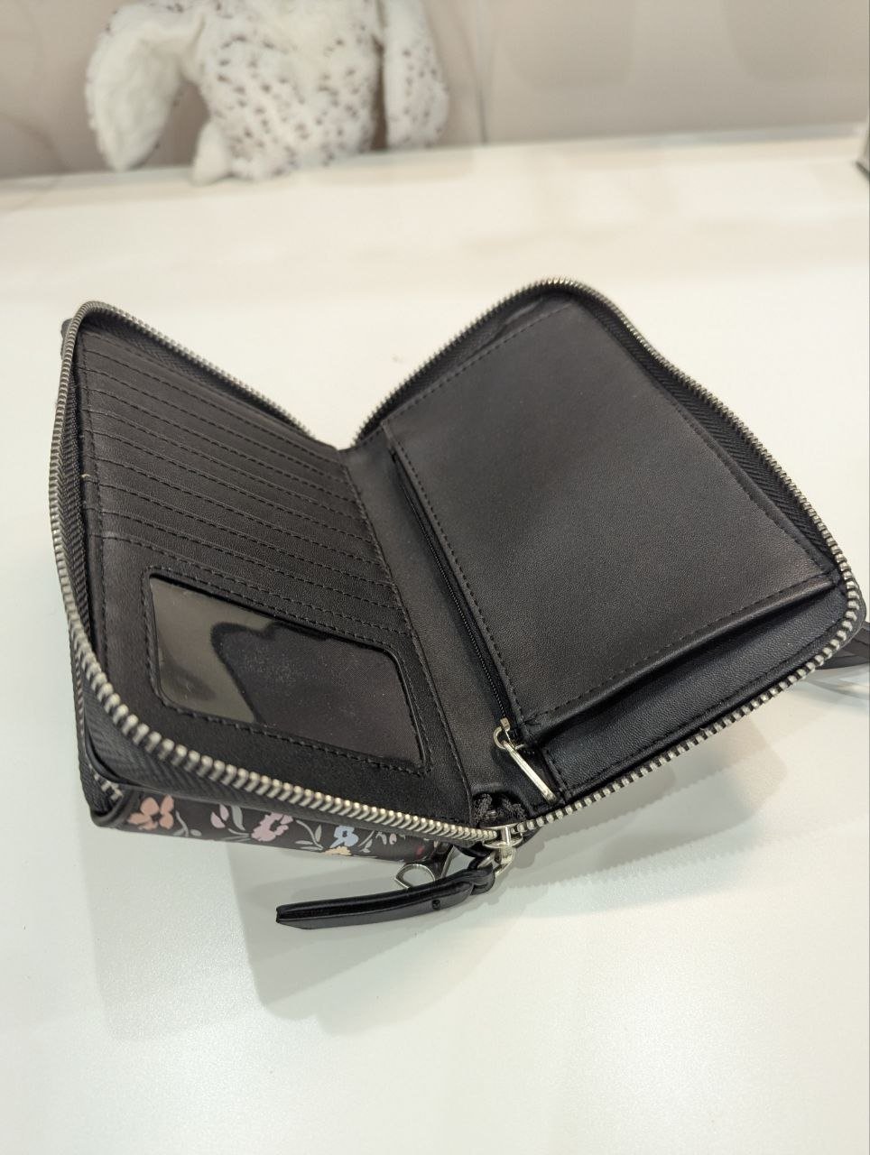 Black leather wallet with a zipper on the front. The wallet is open, revealing the interior. The exterior of the wallet is
