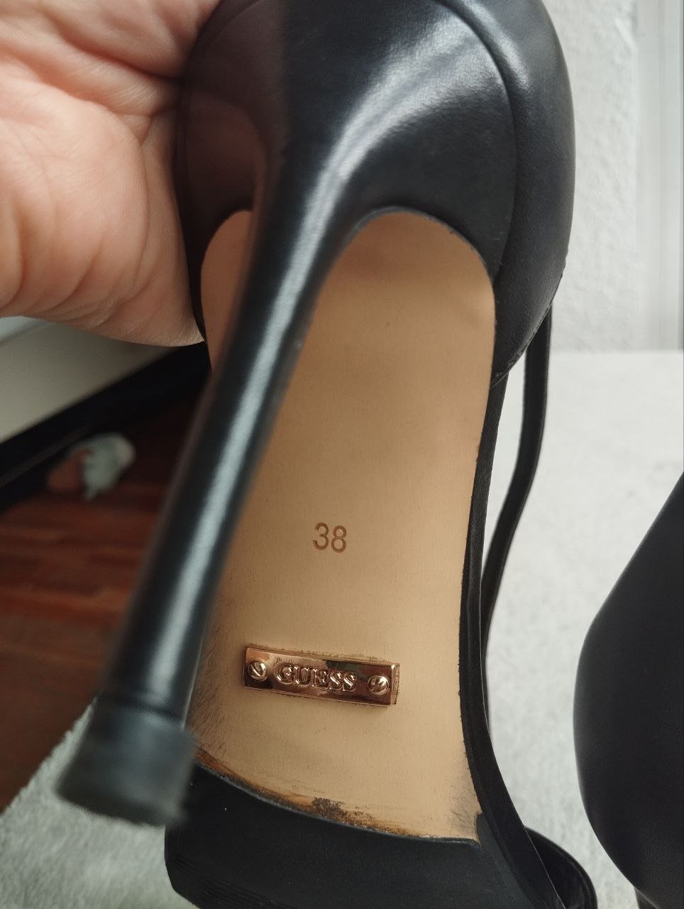 Close-up of a black high-heeled shoe. The shoe has a pointed toe and a stiletto heel. The heel is approximately 38 inches