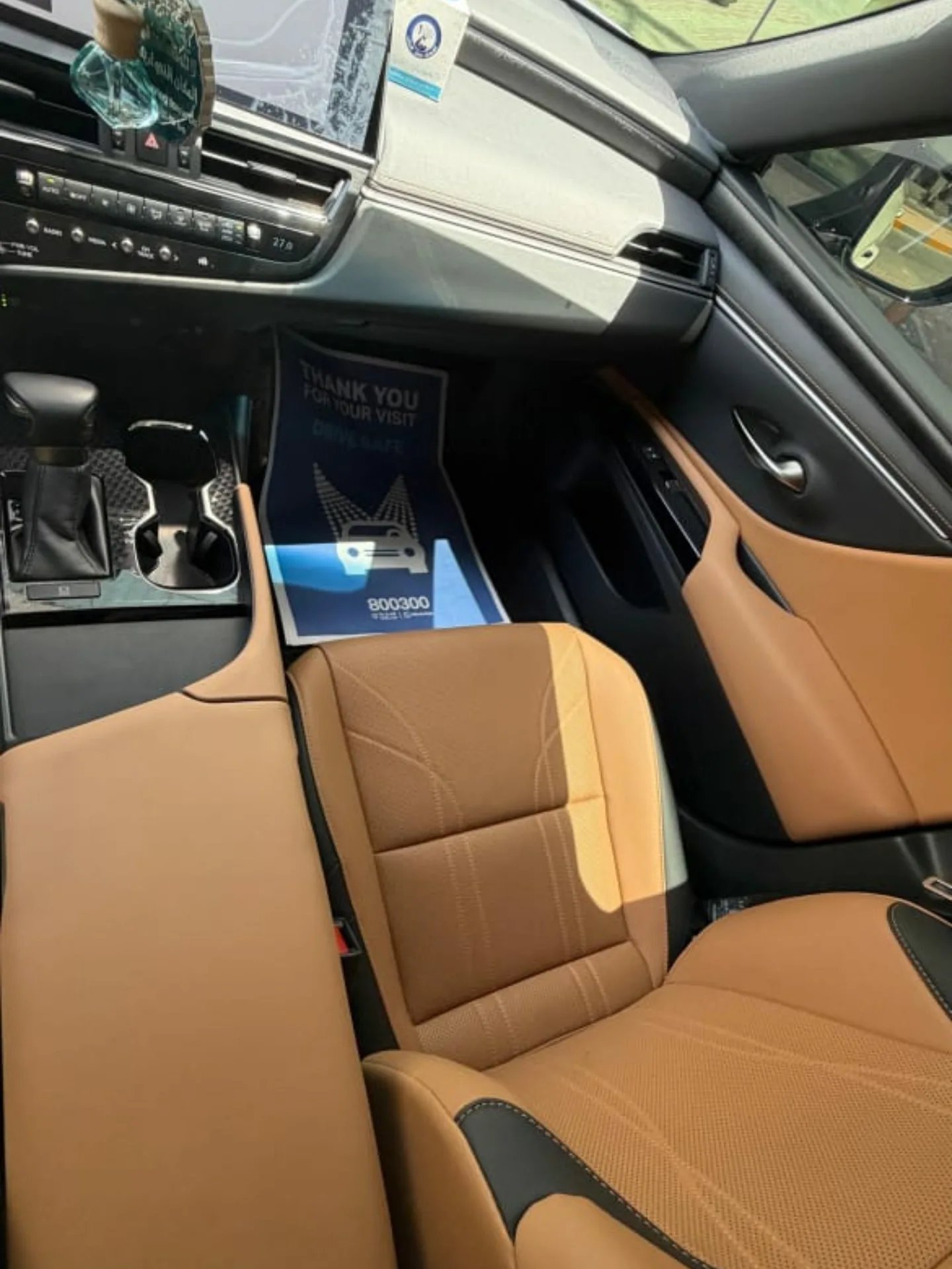 Interior of a car, specifically the driver's seat. The car has a beige leather seat with black stitching. The dashboard is
