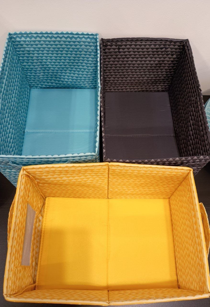 Three rectangular storage baskets with handles. The first basket on the left is blue with a diamond pattern, the second