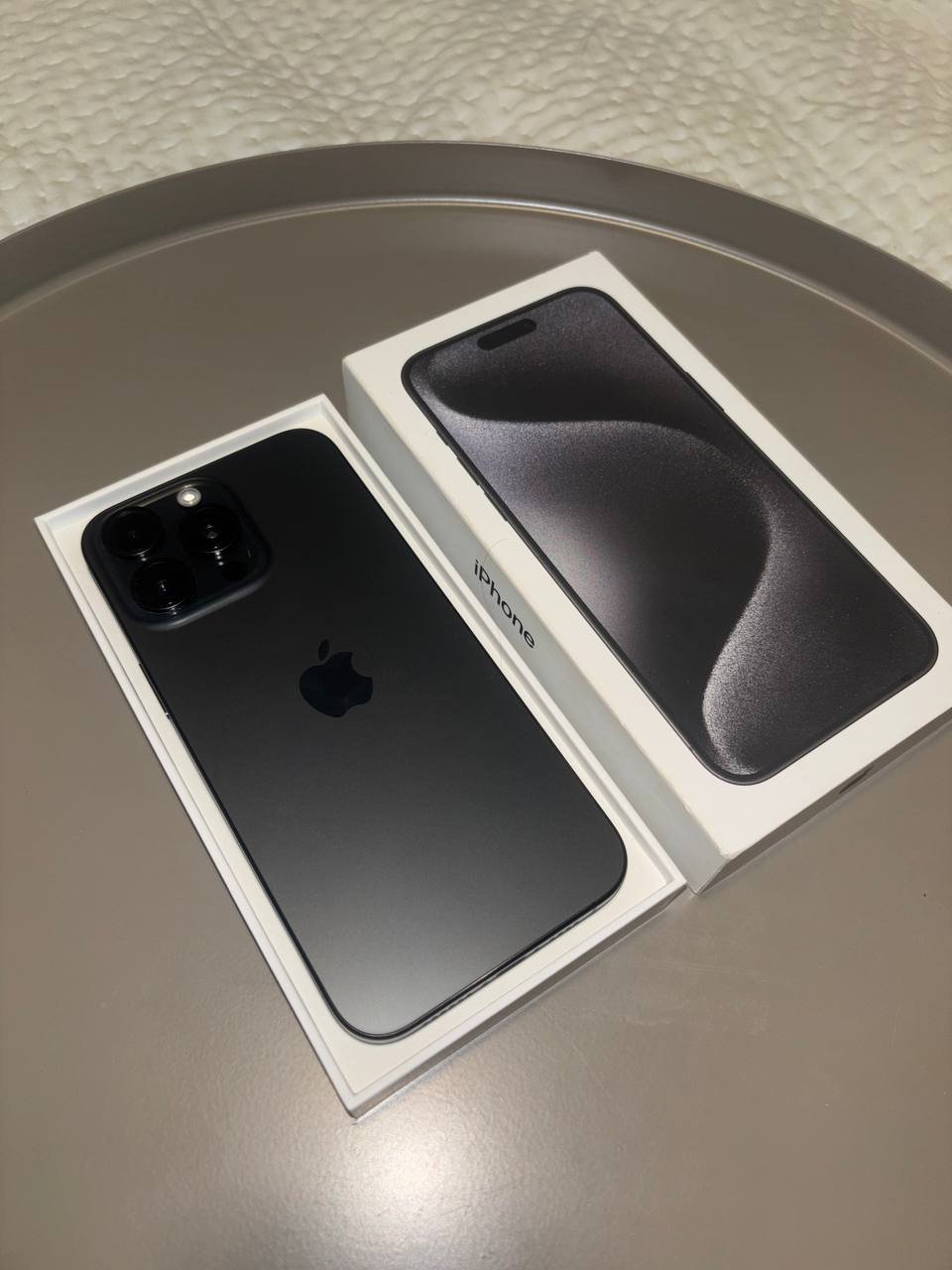 IPhone 11 Pro Max in its original packaging. The phone is black in color and is placed on a white surface with a circular
