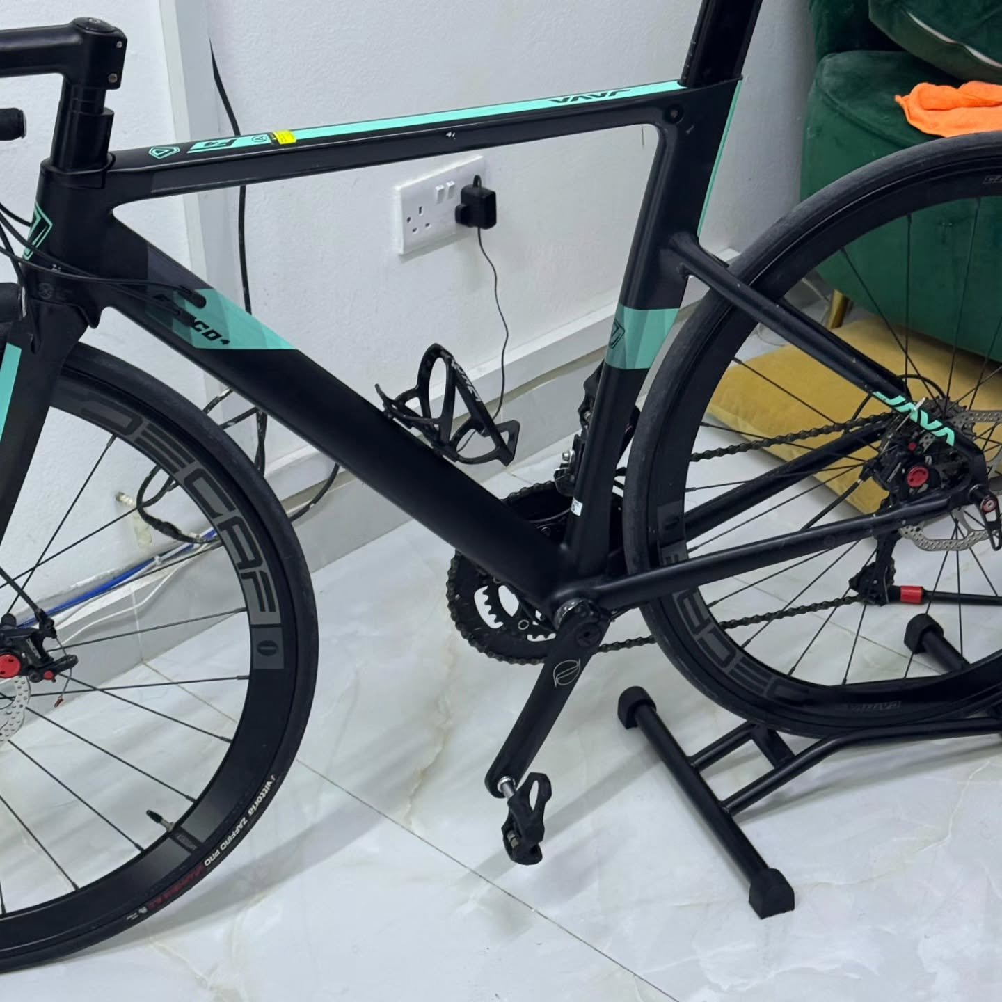 Black and green bicycle leaning against a white wall in a room. The bike has a black frame with green accents and a black