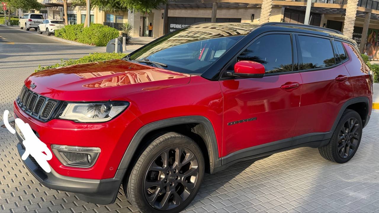 Red Jeep Compass SUV parked on a cobblestone street. The car is a four-door SUV with a sleek and modern design. It has a