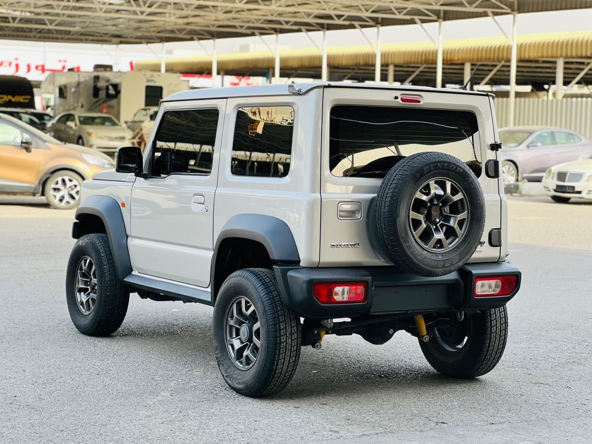 Silver Jeep Wrangler parked in a parking lot. The Jeep is facing towards the right side of the image and is positioned at an