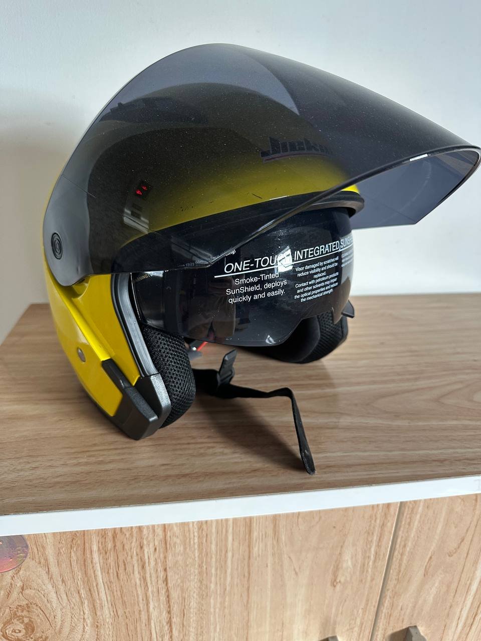 Black and yellow motorcycle helmet with a visor. The helmet is resting on a wooden surface. The visor is transparent and