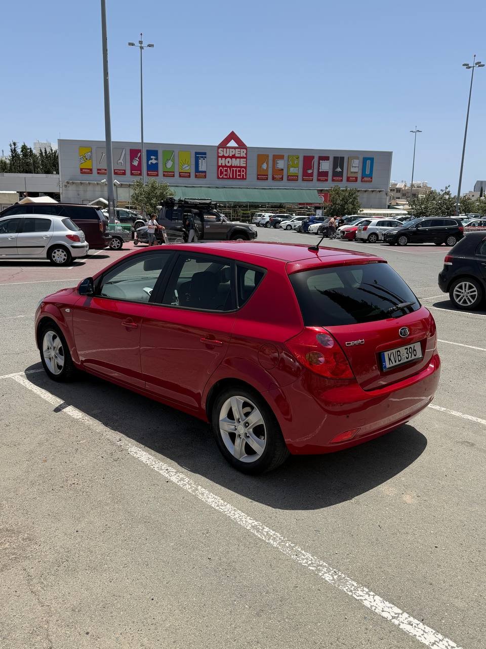 Red car parked in a parking lot. The car is a hatchback model with a sleek design and silver alloy wheels. It is parked in