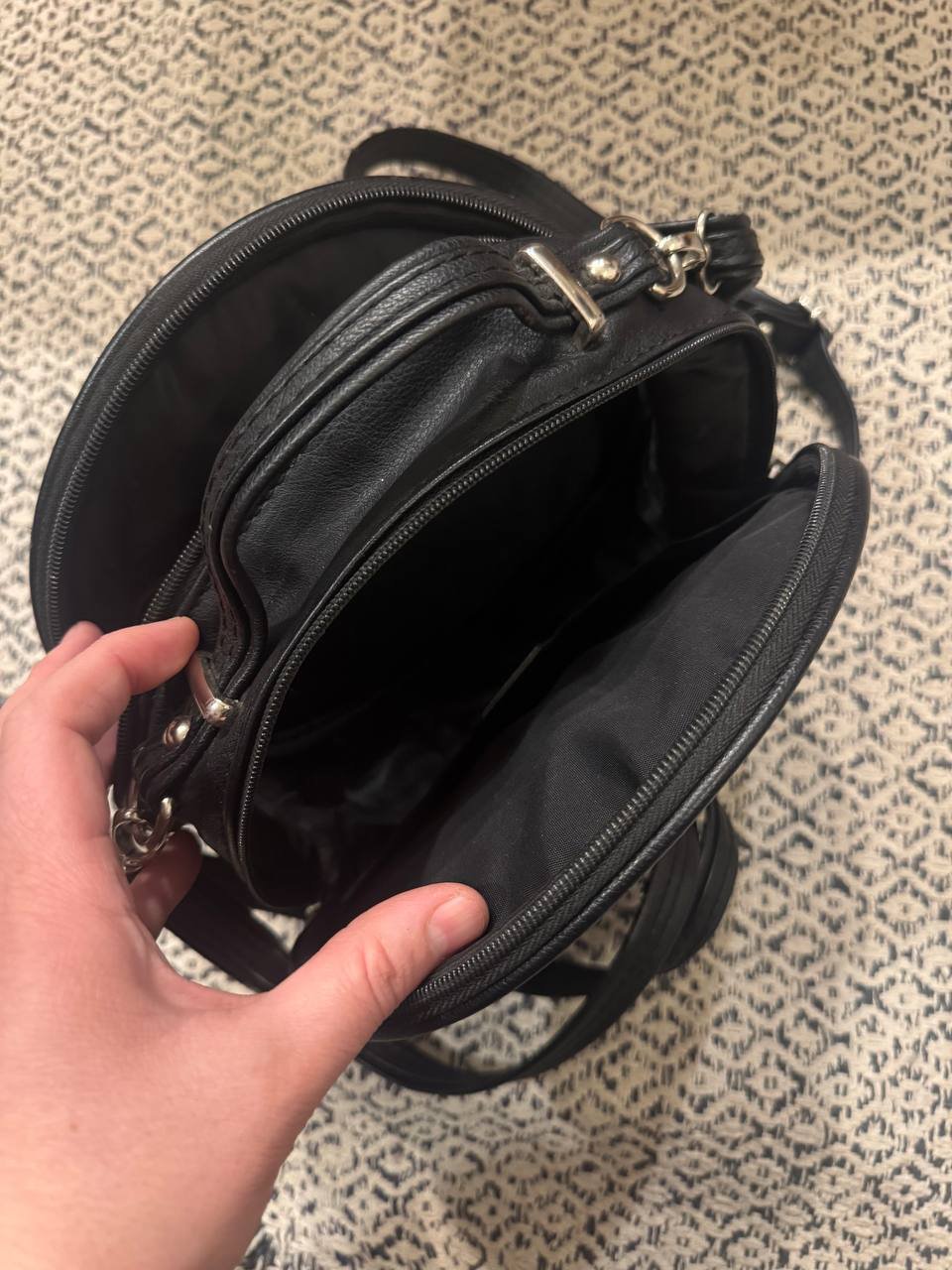 Hand holding a black handbag. The handbag is open, revealing the interior of the bag. The bag appears to be made of leather