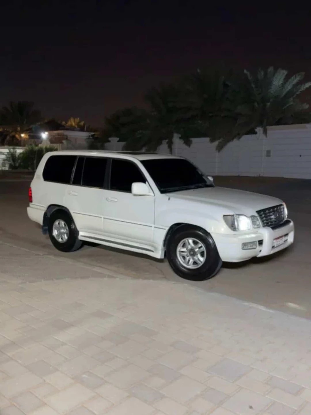 White SUV parked in a driveway at night. The car is a four-door SUV with a sleek design and chrome accents. It has a sunroof