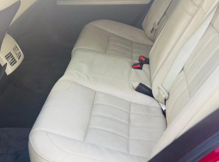 Back seat of a car. The seat is beige in color and appears to be made of leather. It has a seatbelt attached to it with a